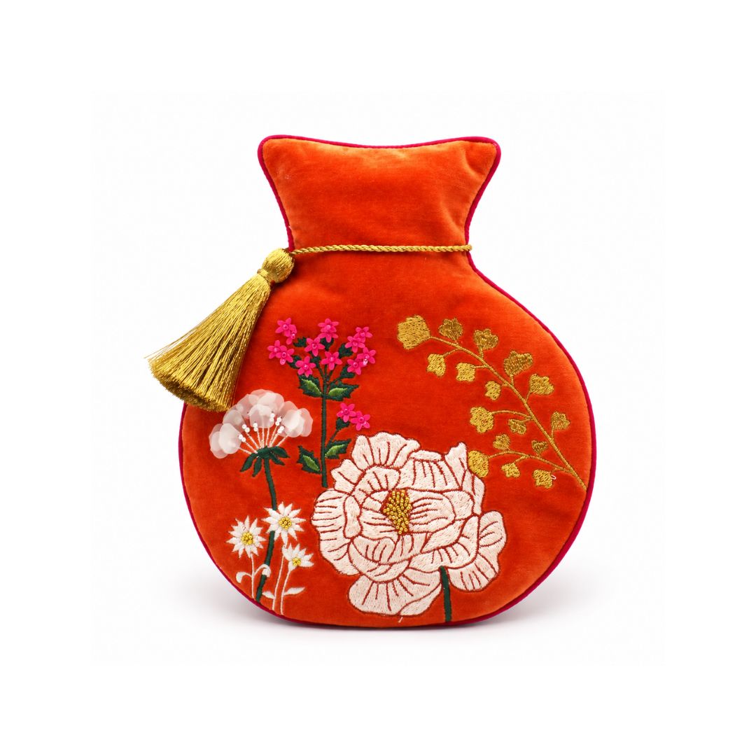 A red velvet hot water bottle cover with embroidered flowers and a gold tassel, shown on a plain white background.