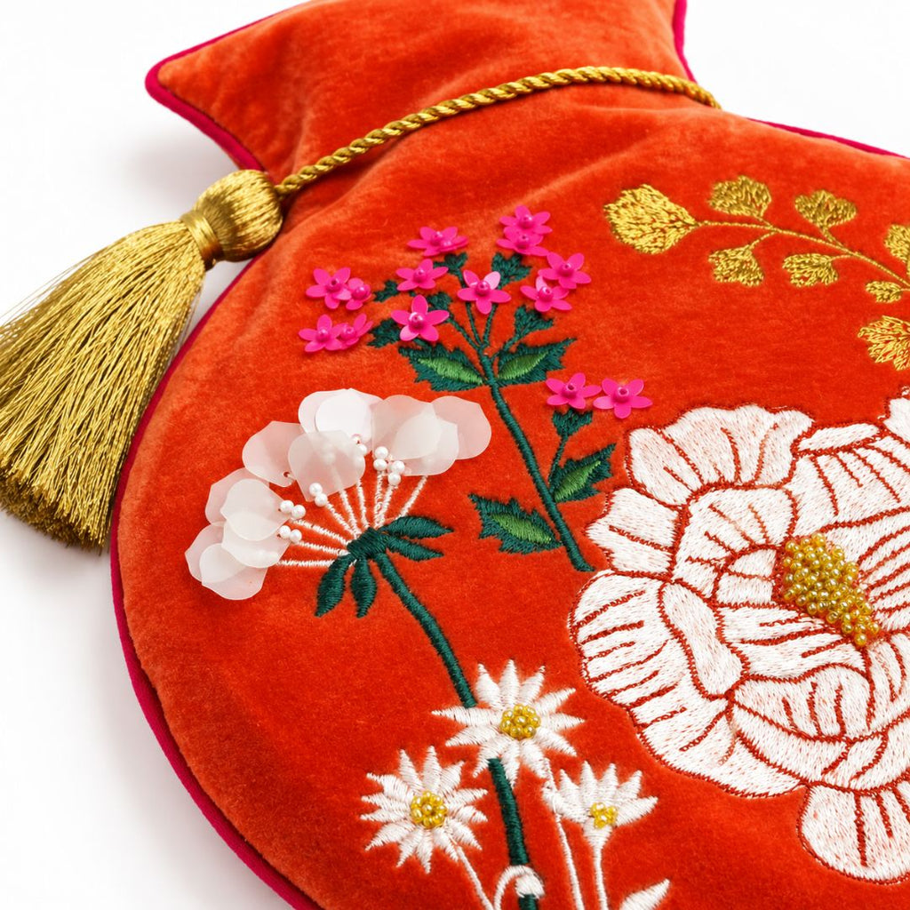 A close-up of a red velvet hot water bottle cover featuring intricate floral embroidery with pink, white, and green flowers, a gold tassel, the best customized gift and gifts for her and for him from Inna Carton online shop Dubai, UAE!
