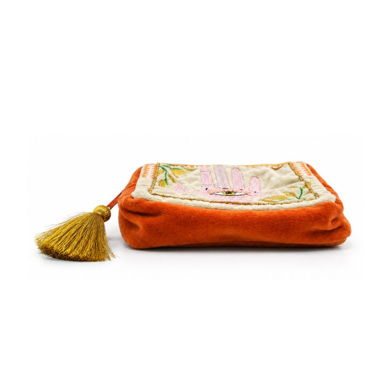 An orange velvet pouch with a gold tassel and a cream-colored embroidered flap featuring pink bunny motifs, set against a plain white background.