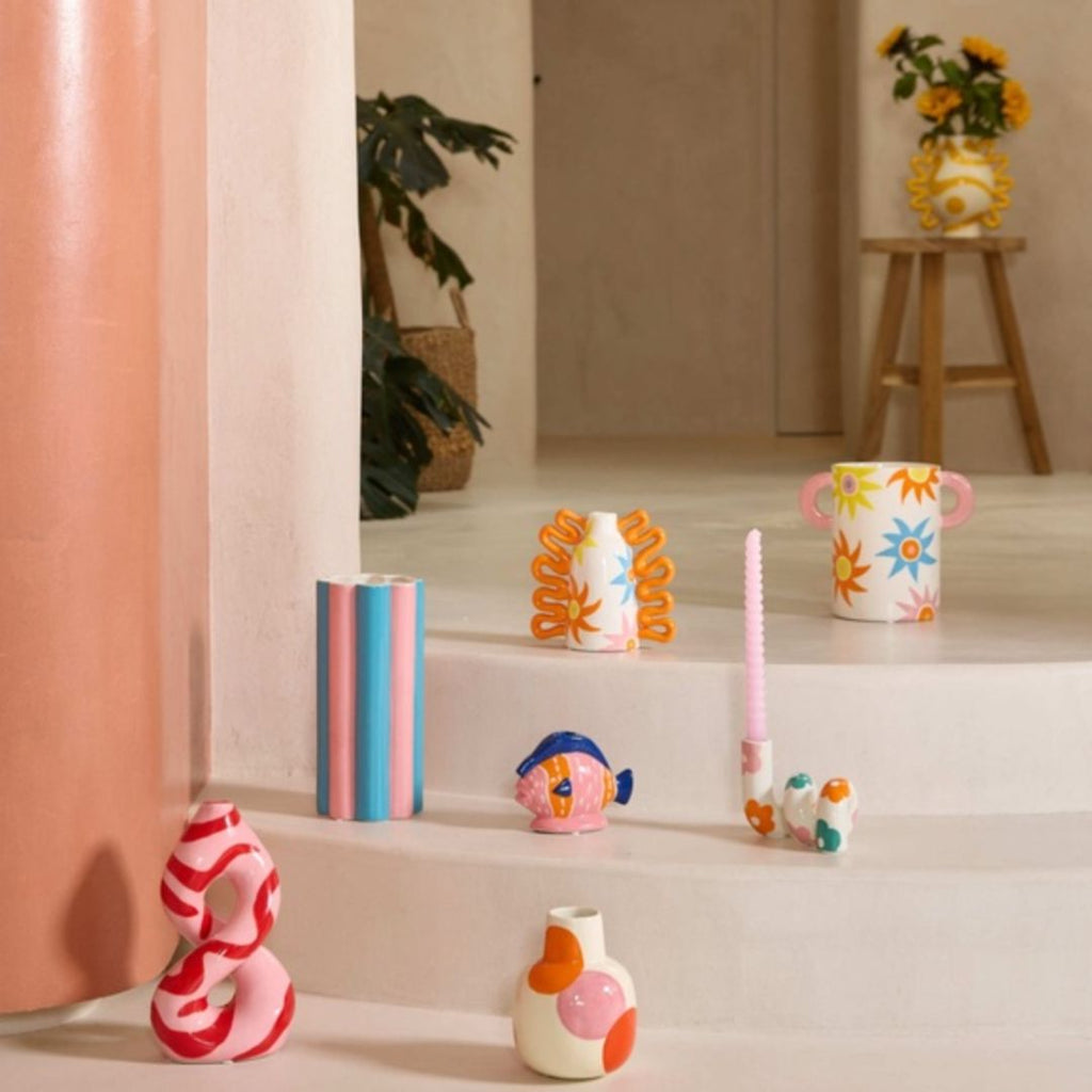 A collection of colorful, hand-painted ceramic vases and cups displayed on white steps in a modern, minimalist interior setting.